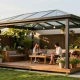 Freistehende Terrassenüberdachung im modernen Design, umgeben von blühenden Pflanzen.